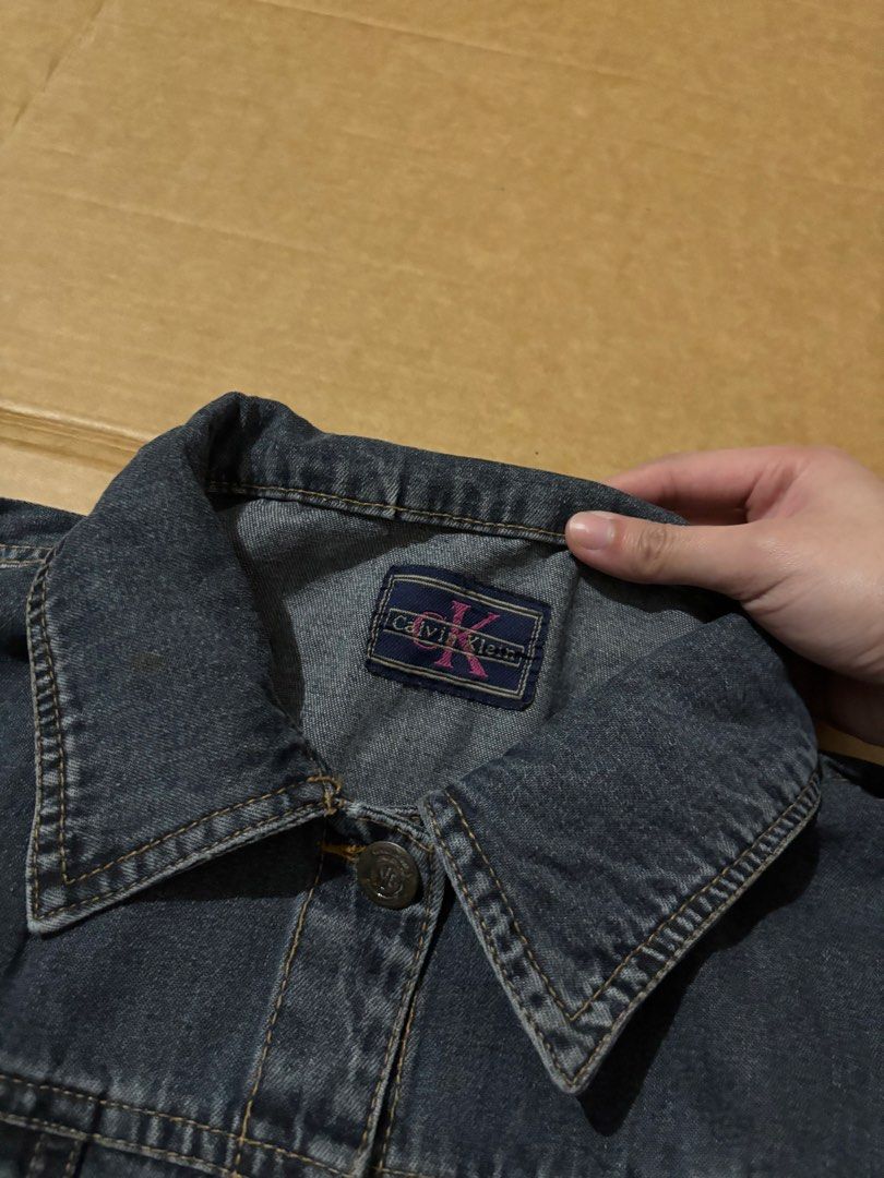 Calvin Klein dark grey denim jacket (Category: Coats, Jackets and Outerwear) located in Manila. Submitted by aysshxx (Listing ID 1470422371, Image 2). Description: - Brand: Calvin Klein - Color/Wash: Dark grey acid wash - Closure: Classic button-up front with branded metallic hardware - Pockets: Two chest pockets with button flaps - Details: Collar neckline and stylish contrast stitching throughout - Condition: Excellent / Ready to wear.
