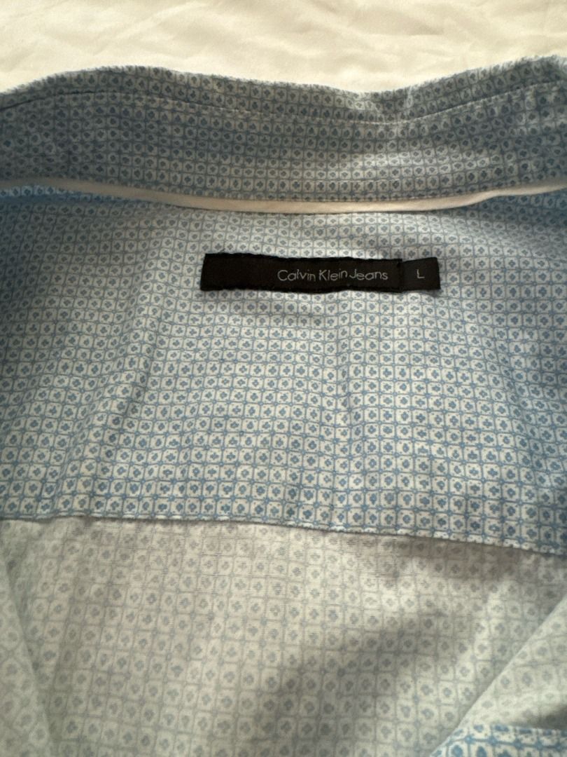 Calvin Klein Jeans Light Blue Patterned Long Sleeve Shirt Large (Category: Longsleeves) located in Cebu City. Submitted by _t.rix (Listing ID 1470382931, Image 3). Description: - Brand: Calvin Klein Jeans - Color: Light blue with subtle geometric micro-print - Style: Long sleeves, classic collar, front button closure - Details: Small black logo tag near the bottom hem - Fit: Standard fit - Versatility: Great for casual wear or dressing up.