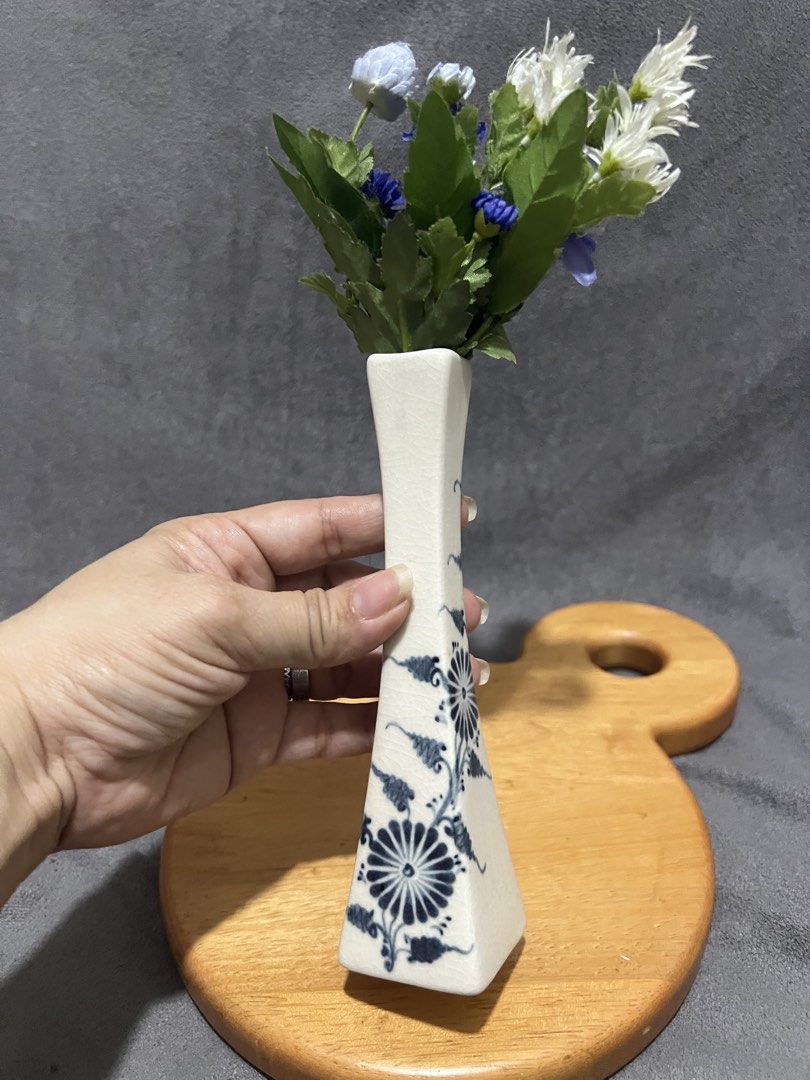 Ceramic Bud Vase flower not included (Category: Vases & Decorative Bowls) located in Las Pinas. Submitted by maple0305 (Listing ID 1470497971, Image 3). Description: - Type: Ceramic bud vase with square base and narrowing neck - Design: Classic blue and white floral painting with a crackle glaze finish - Inclusions: Comes with a small artificial flower arrangement (blue, purple, white with green stems) - Height: Approx. 20 cm total (including flo