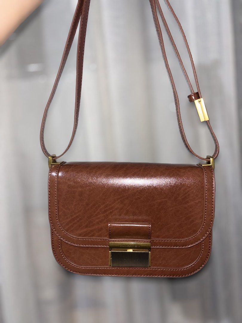 Charles & Keith Charlot Bag Dark Brown (Category: Cross-body Bags) located in Pasay City. Submitted by sggma (Listing ID 1470491274, Image 3). Description: - Brand: Charles & Keith - Style: Charlot Bag (Classic saddle shape) - Color: Dark Brown with brushed gold hardware - Closure: Secure push-lock - Strap: Includes adjustable shoulder strap - Condition: Clean inside and out, very well maintained - Features: Rich texture finish, spacious enough f