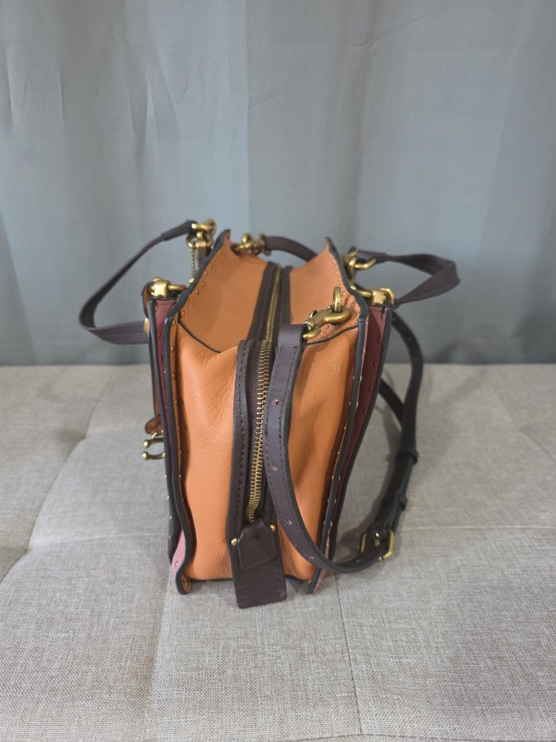Coach Rogue Bag (Category: Luxury Bags & Wallets) located in Binan City. Submitted by karosellescloset (Listing ID 1470422110, Image 2). Description: Coach 1941 Rogue Bag featuring a studded colorblock design in leather and suede trim. ​Key defining features include: ​Model Line: Coach 1941 Rogue (Satchel / Tote). ​Design Details: Colorblocked leather panels (dark brown center body, pink trim, and orange/peach side gussets), brass hardware, borde