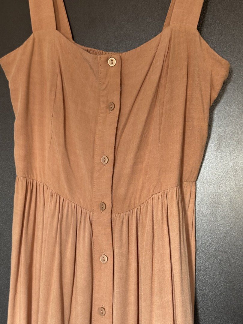 Coco Cabaña Brown Button-Down Summer Dress (Category: Dresses) located in Dasmarinas. Submitted by akelvin23 (Listing ID 1470429557, Image 2). Description: - Brand/Style: Coco Cabaña midi dress - Color: Neutral brown - Details: Square neckline, thick straps, gathered bodice, and matching front buttons - Fit: Fitted waist with a smocked back panel for flexibility - Skirt: Tiered, flowy design with a slight high-low hem - Fabric: Lightweight and te