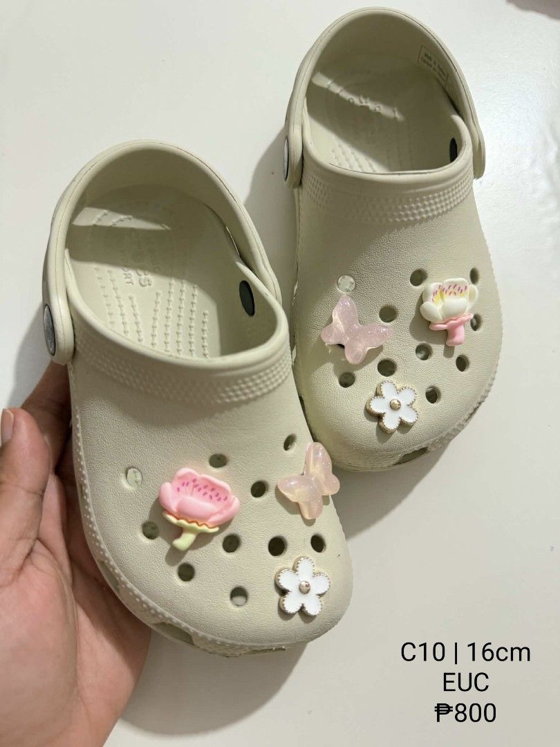 Crocs C10 16cm with Charms (Category: Babies & Kids Fashion) located in San Fabian. Submitted by hbrst1998 (Listing ID 1470357304, Image 1). Description: - Brand: Crocs - Color: Bone / Off-white - Size: C10 (Measures 16cm) - Condition: Gently worn, very clean uppers and treads - Inclusions: Decorated with cute pink butterfly and flower Jibbitz charms - Ready for its next little owner!.