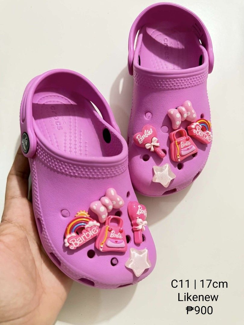 Crocs C11 17cm with Jibbitz Charms (Category: Babies & Kids Fashion) located in San Fabian. Submitted by hbrst1998 (Listing ID 1470358880, Image 1). Description: - Brand/Style: Pink Crocs clogs for kids - Size: C11 (17cm measurement) - Charms: Decorated with cute Barbie-themed Jibbitz (rainbow, pink handbag, star, bow, and Barbie logo) - Features: Easy slip-on style with a secure heel strap - Condition: Great pre-loved condition - Perfect for lit