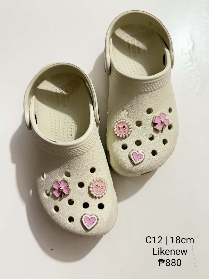 Crocs C12 18cm with Jibbitz charms (Category: Babies & Kids Fashion) located in San Fabian. Submitted by hbrst1998 (Listing ID 1470355553, Image 1). Description: - Brand: Crocs - Color: Bone White - Size: C12 (18cm) - Condition: Like new, worn only once or twice, super clean soles - Extras: Pre-styled with cute pink and gold charms (hearts, flowers, and pearls) - Features: Easy slip-on design with secure heel straps.