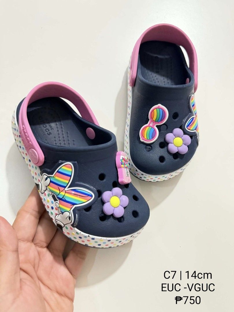 Crocs C7 Minnie Mouse Kids Clogs 14cm (Category: Babies & Kids Fashion) located in San Fabian. Submitted by hbrst1998 (Listing ID 1470358535, Image 1). Description: - Size: C7 (approx. 14cm) - Color: Navy blue with pink back strap and polka dot midsole trim - Design: Minnie Mouse graphics, flower charms, and colorful sunglasses charms - Features: Slip-on style with pivoting heel straps - Condition: Clean footbeds, very little sign of wear on trea