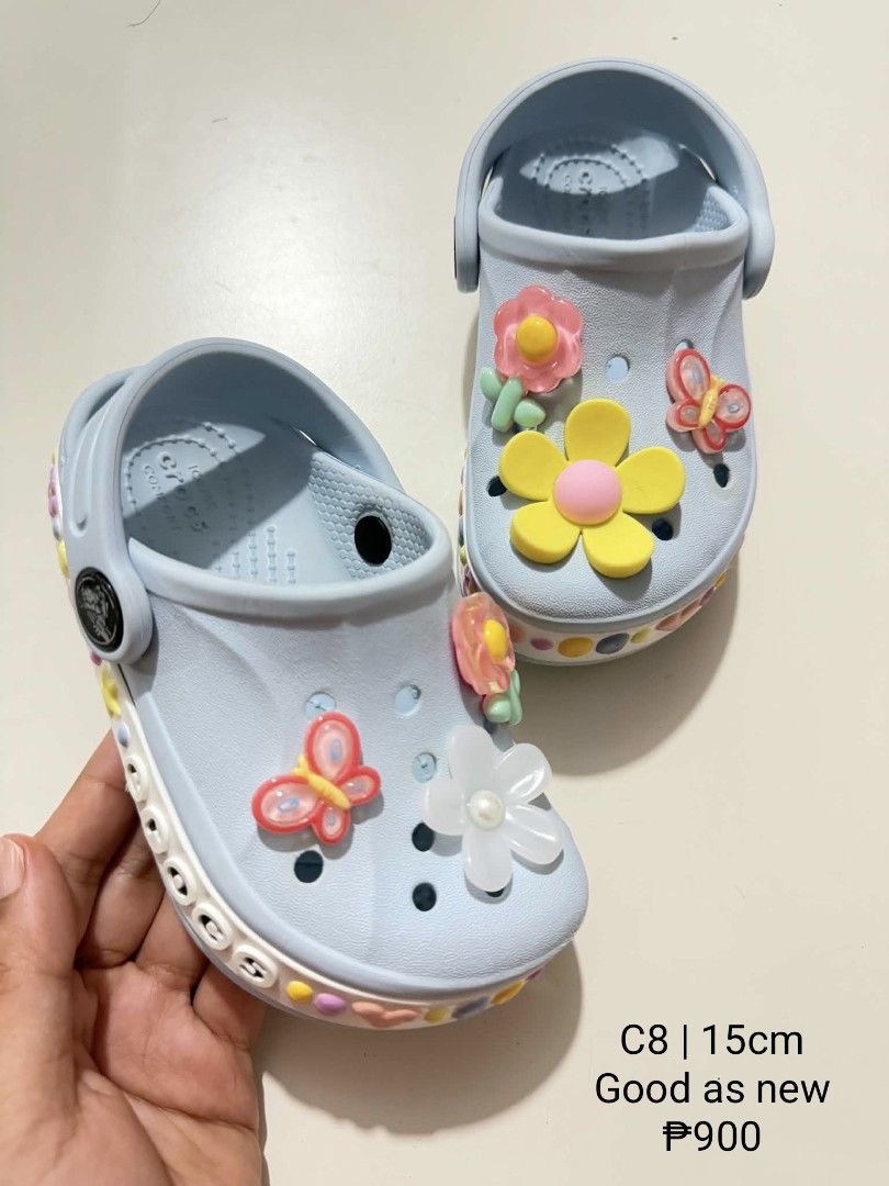 Crocs C8 15cm Light Blue with Charms (Category: Babies & Kids Fashion) located in San Fabian. Submitted by hbrst1998 (Listing ID 1470359098, Image 1). Description: - Size: C8 (approx. 15cm) - Color: Light blue with a white midsole and colorful dot patterns - Design: Slip-on with pivoting heel straps and Crocs lettering - Extras: Pre-decorated with cute flower and butterfly charms - Condition: Worn very lightly, soles are clean and practically unt