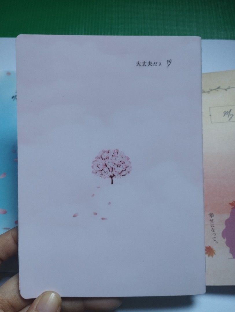 Cute Cherry Blossom Notebook Japanese Aesthetic Diary (Category: Stationery & School Supplies) located in San Mateo. Submitted by diana_01.tree (Listing ID 1470350755, Image 2). Description: - Cover: Soft pink with a charming cherry blossom tree illustration, pocket size - Back: Features Japanese text and a cute small heart - Pages: Pretty floral borders at the top, watercolor wash, and with designs inside pages - Design: Slim and lightweight, ea