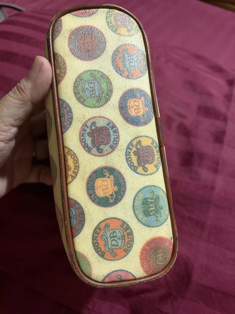 Dooney & Bourke Multicolored Coin Print Cosmetic Pouch (Category: Purses & Pouches) located in Las Pinas. Submitted by ces0427 (Listing ID 1470470692, Image 2). Description: - Authentic Dooney & Bourke cosmetic pouch - Multicolored circular coin and crest print on a cream base with brown trim - Secure zip-top closure with dark red zipper fabric - Bright red fabric interior lining equipped with a convenient slip pocket - Structured base to hold it