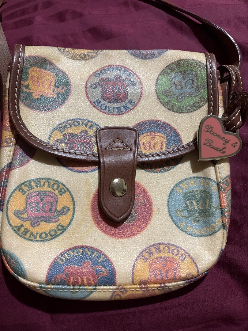 Dooney & Bourke Multicolored Logo Crossbody Bag (Category: Cross-body Bags) located in Las Pinas. Submitted by ces0427 (Listing ID 1470472561, Image 3). Description: - Authentic Dooney & Bourke crossbody bag - Cream fabric with vibrant all-over logo seal prints - Premium brown leather trim and matching adjustable strap - Secure front flap with snap closure - Includes adorable pink heart-shaped metal charm - Perfect everyday chic bag!.