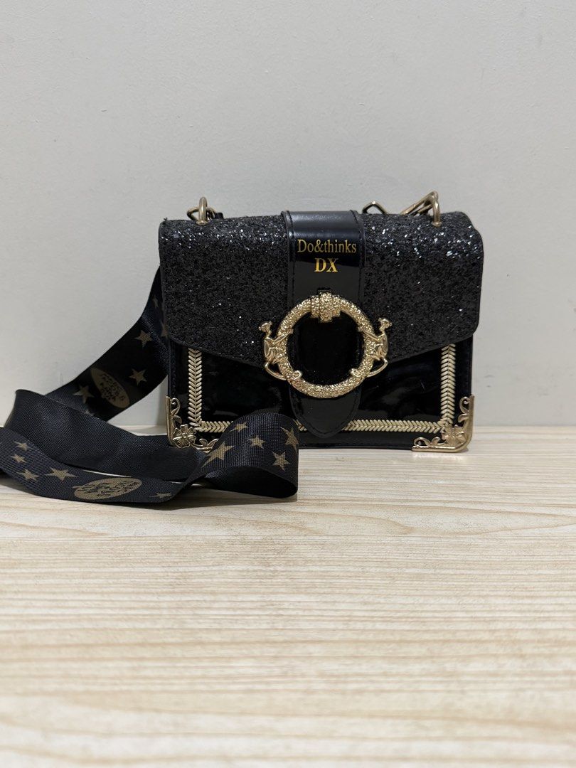 Do&thinks DX Black Glitter Crossbody Handbag (Category: Cross-body Bags) located in Magalang. Submitted by xeevain (Listing ID 1470457809, Image 1). Description: - Color & Finish: Black glitter with glossy patent trim - Hardware: Elegant gold-tone with an ornate round clasp closure - Strap: Matching black strap adorned with gold star patterns - Size: Compact and lightweight - Perfect For: Nights out, parties, and special occasions ***CLAIM FOR FR