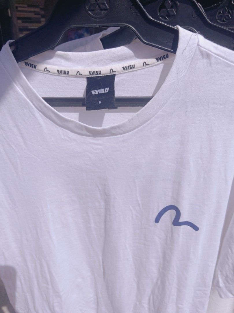 Evisu White Graphic T-Shirt Size M (Category: Tshirts & Polo Shirts ) located in Gapan. Submitted by athenascarlet (Listing ID 1470480993, Image 2). Description: - Color: White - Size: M (Regular fit) - Material: 100% Cotton - Design: Blue seagull logo on chest, large Evisu lettering graphic with hanging lines on the back - Details: Branded collar tape and black Evisu neck tag - Condition: Brand new / Excellent quality.