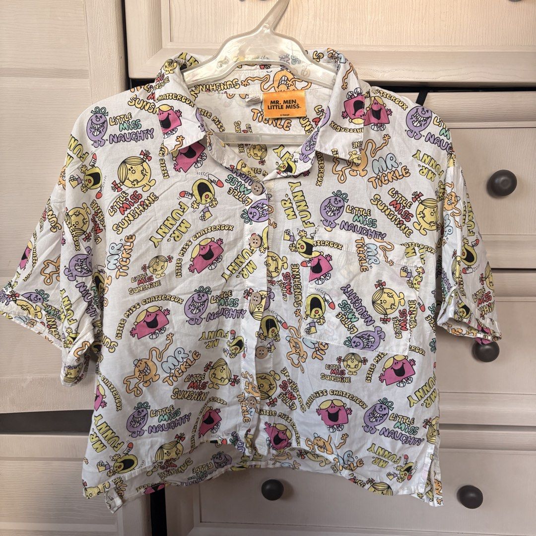 Graphic Polo Top (Category: Shirts) located in Makati City. Submitted by iu__00 (Listing ID 1470444451, Image 1). Description: - Design: Fun all-over print featuring classic Mr. Men and Little Miss characters like Mr. Tickle and Little Miss Sunshine - Color: White base with vibrant, colorful cartoon graphics - Features: Classic collar, short sleeves, front button closure, and a single chest pocket - Size: XS on tag (runs big) - Condition: Great f