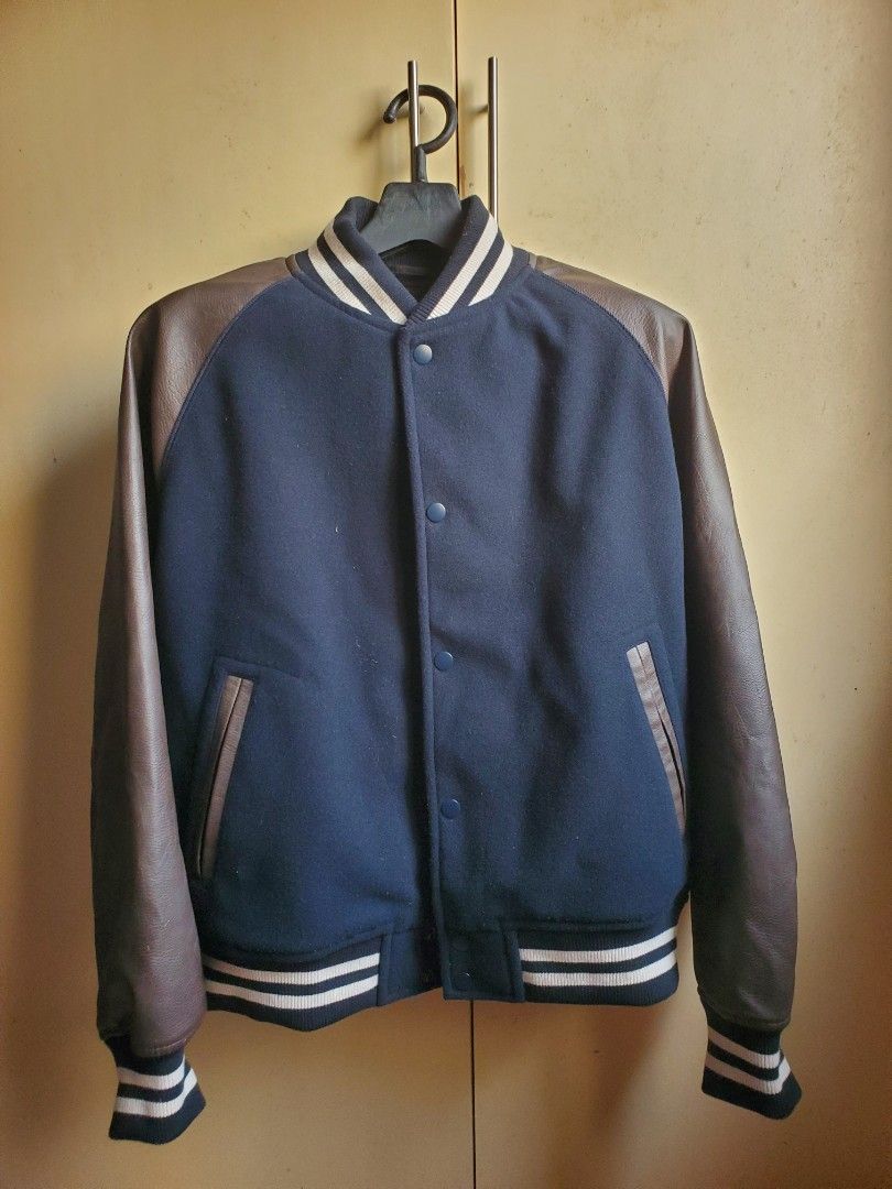 GU Cozy Melton Stadium Jumper (Brown) (Category: Coats, Jackets and Outerwear) located in Manila. Submitted by seanceman (Listing ID 1470381803, Image 1). Description: - Classic college-style varsity jacket - Navy blue wool body with contrast brown faux leather sleeves - Dark blue and white striped ribbed collar, cuffs, and hem - Convenient snap button front closure - Two front welt pockets with trim - Stylish and cozy outerwear for chilly days.