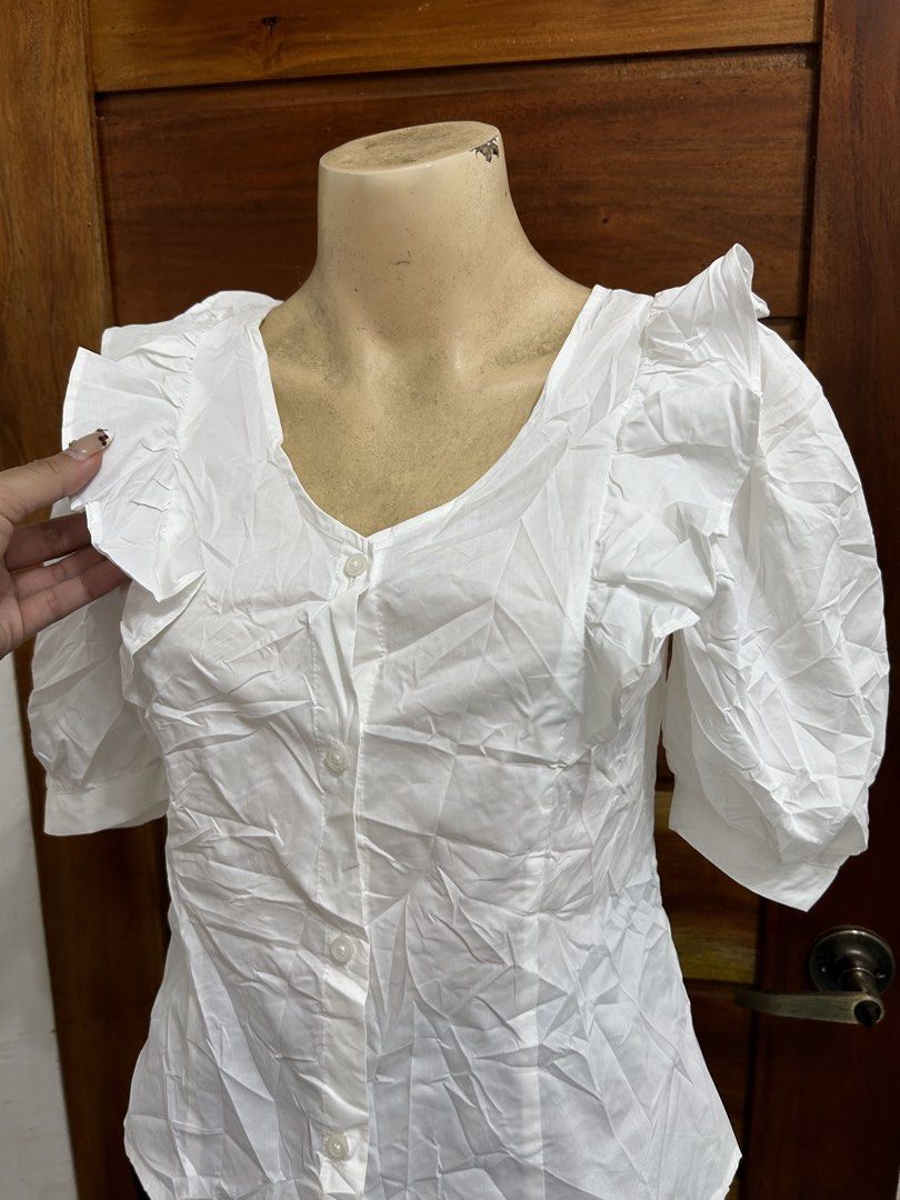 GU White Ruffle Puff Sleeve Button-Up Blouse Size S (Category: Blouses) located in Valencia. Submitted by crizzagella20 (Listing ID 1470545796, Image 3). Description: - Brand: GU - Size: Small - Color: White - Material: Cotton and polyester blend - Design: V-neck with front buttons - Details: Short puff sleeves with ruffle trim along shoulders and neckline - Condition: Clean and ready to wear.