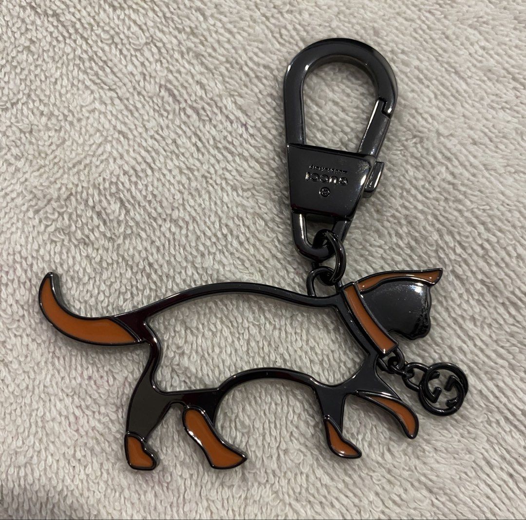 Gucci Cat Keychain Bag Charm (Category: Charms) located in Muntinlupa City. Submitted by mj.finds (Listing ID 1470461997, Image 1). Description: - Gucci cat keychain - Gunmetal hardware with orange enamel accents - Features a dangling Interlocking G logo charm - Engraved Gucci branding on the clasp - Heavy metal construction with a super sturdy hook - Great for styling handbags or using as a keyring.