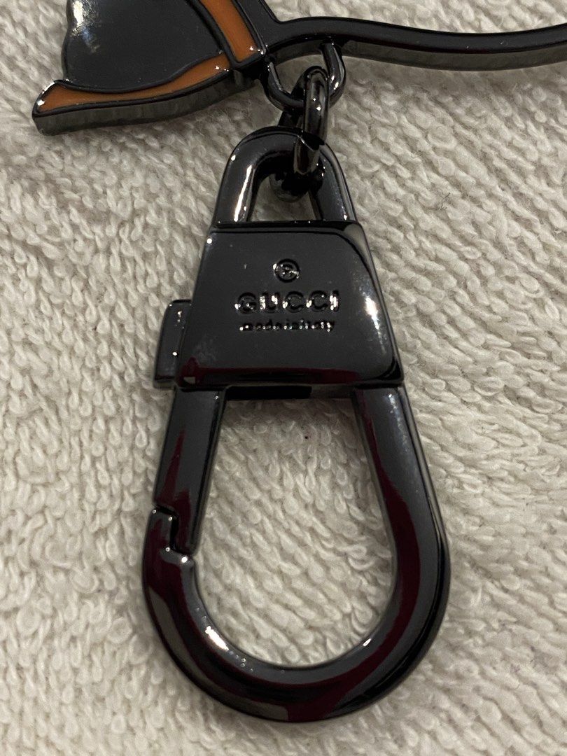 Gucci Cat Keychain Bag Charm (Category: Charms) located in Muntinlupa City. Submitted by mj.finds (Listing ID 1470461997, Image 3). Description: - Gucci cat keychain - Gunmetal hardware with orange enamel accents - Features a dangling Interlocking G logo charm - Engraved Gucci branding on the clasp - Heavy metal construction with a super sturdy hook - Great for styling handbags or using as a keyring.