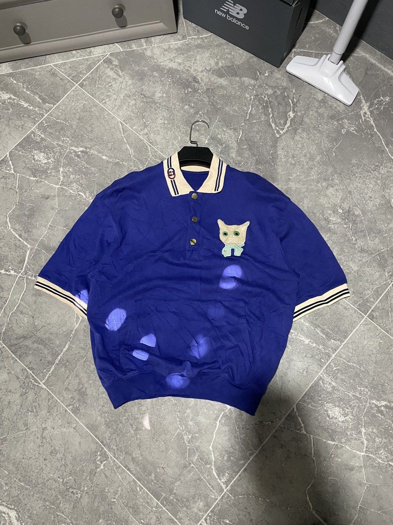 Gucci Cat Patch Blue Polo Shirt (Category: Tshirts & Polo Shirts ) located in Buenavista. Submitted by ivoperez27 (Listing ID 1470403768, Image 1). Description: - Brand: Gucci - 23 width 27 length - Color: Deep royal blue with cream and striped contrasting trims - Details: Embroidered interlocking G logo on collar, gold-tone Gucci-stamped buttons, and cute embroidered cat face patch with a light blue bow - Pockets: Front kangaroo pocket - Fit: Re