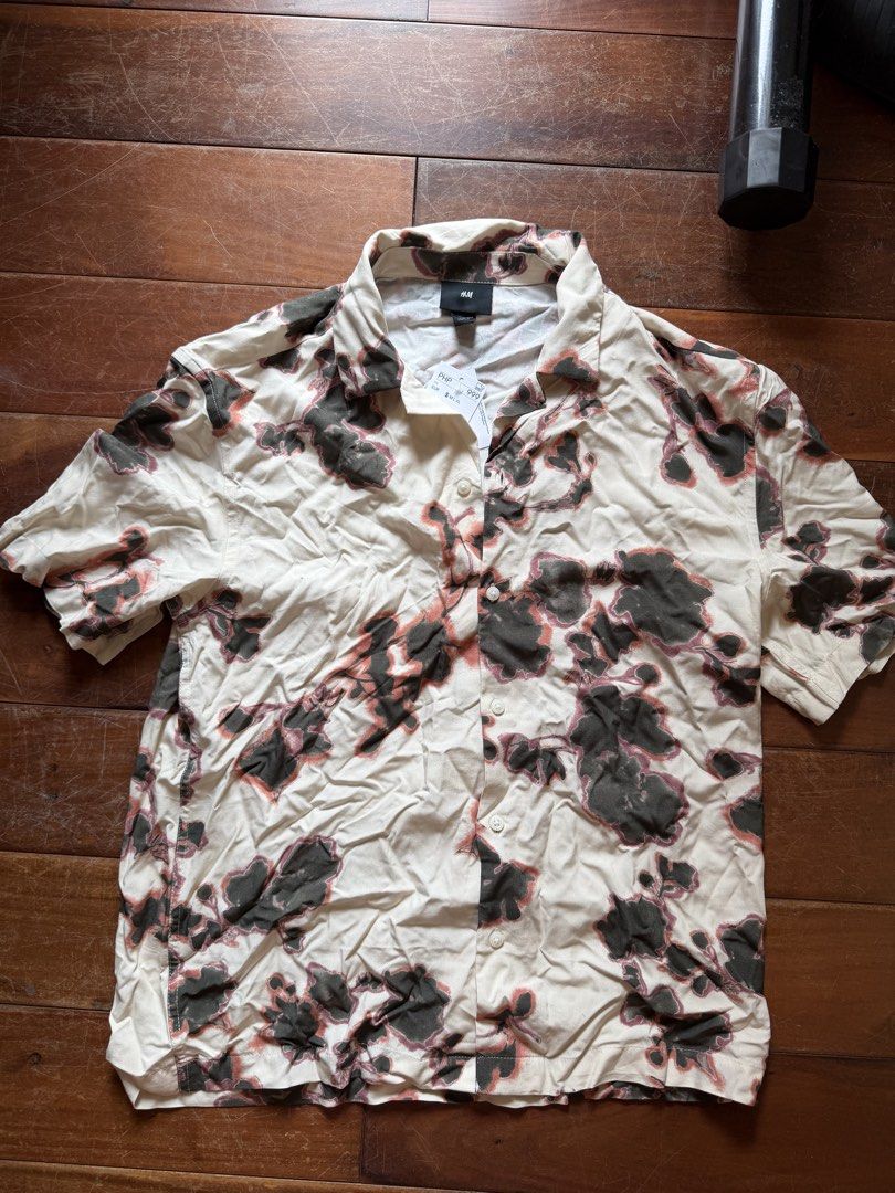H&M Floral Pattern Short Sleeve Shirt (Category: Tshirts & Polo Shirts ) located in Cebu City. Submitted by _iamnicolle (Listing ID 1470423089, Image 2). Description: - Brand: H&M (Brand new with tag) - Style: Short sleeve camp collar button-down - Color/Pattern: Cream base with dark green and reddish floral blotches - Fit: loose fit, lightweight fabric - Details: White front buttons, original price tag still attached.