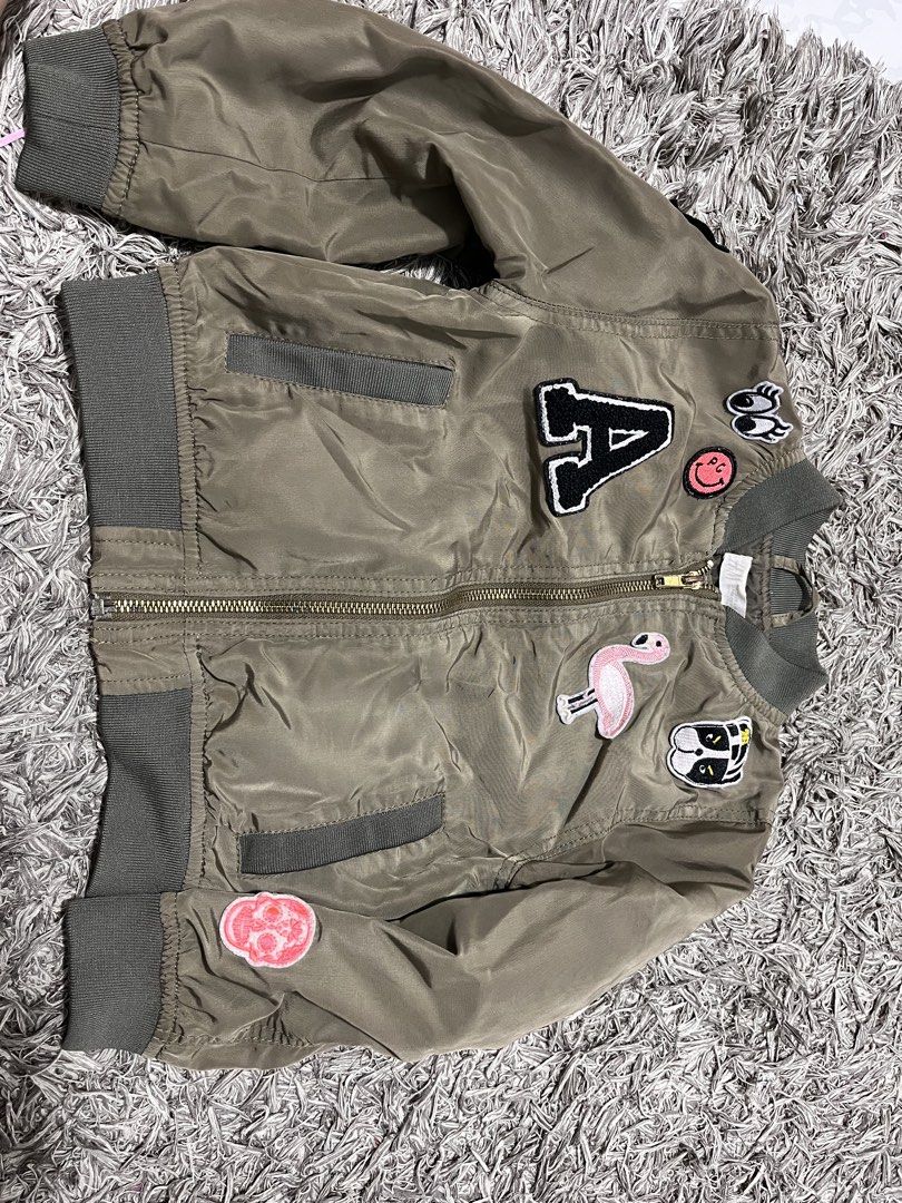 H&M Olive Green Bomber Jacket with Patches (Category: Babies & Kids Fashion) located in Lucena. Submitted by cheapanddealshop (Listing ID 1470550978, Image 1). Description: - Brand: H&M - Color: Olive green - Design: Fun embroidered patches (big letter A, flamingo, skull, smiley face) - Features: Full zip front, side pockets, ribbed collar, cuffs, and hem - Fit: Lightweight youth/kids outerwear with a cool streetwear vibe Excellent Condition No T