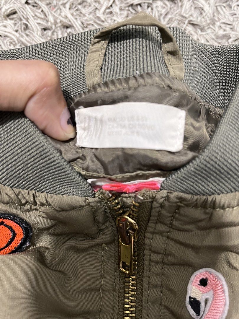 H&M Olive Green Bomber Jacket with Patches (Category: Babies & Kids Fashion) located in Lucena. Submitted by cheapanddealshop (Listing ID 1470550978, Image 2). Description: - Brand: H&M - Color: Olive green - Design: Fun embroidered patches (big letter A, flamingo, skull, smiley face) - Features: Full zip front, side pockets, ribbed collar, cuffs, and hem - Fit: Lightweight youth/kids outerwear with a cool streetwear vibe Excellent Condition No T