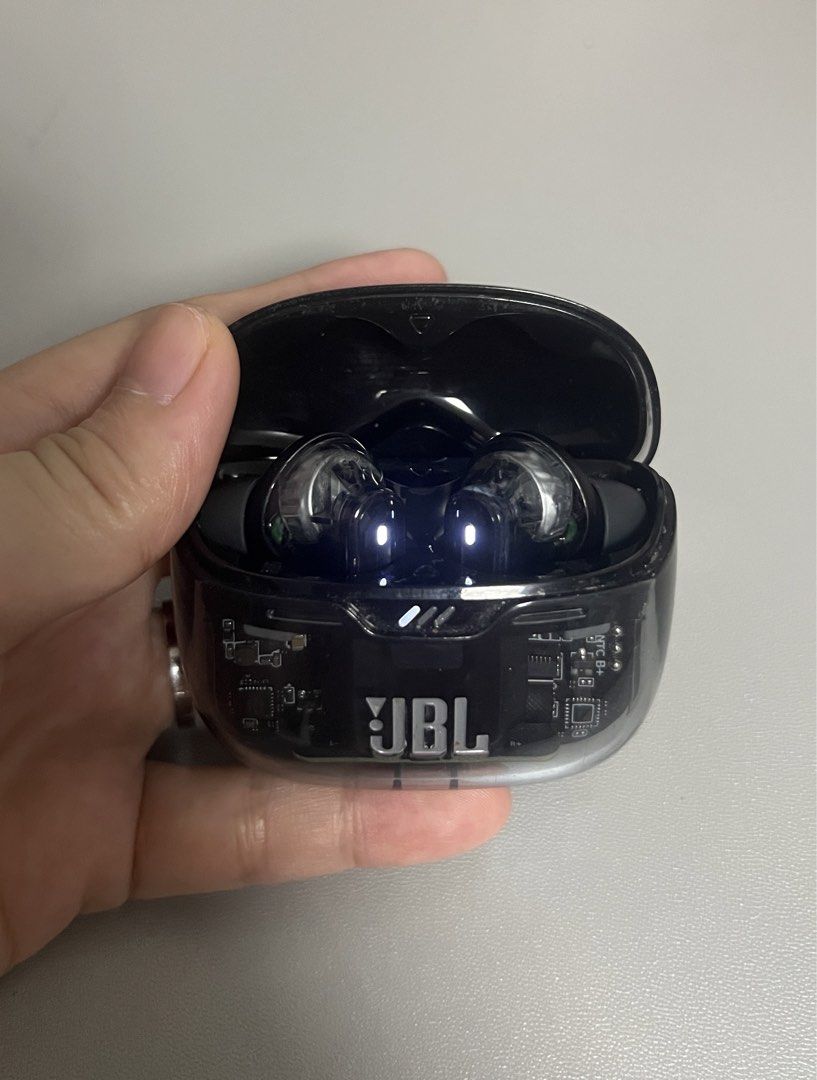 JBL Transparent Wireless Earbuds Charging Case (Category: Earphones) located in Marilao. Submitted by maygomez05 (Listing ID 1470468397, Image 2). Description: - No box included - Transparent black casing and visible circuit board - Features the prominent JBL logo on the front - Stem-style earbuds with glowing blue LED indicator lights - Compact charging case that easily fits in your hand or pocket - Stylish and reliable everyday audio accessory.