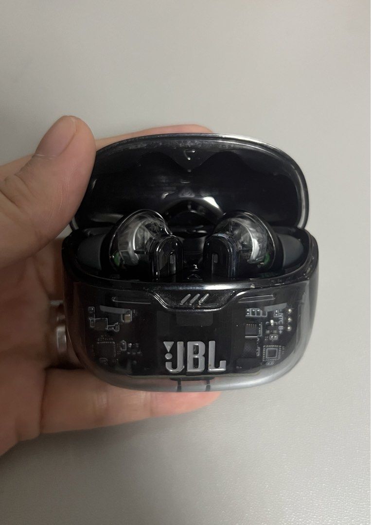 JBL Transparent Wireless Earbuds Charging Case (Category: Earphones) located in Marilao. Submitted by maygomez05 (Listing ID 1470468397, Image 3). Description: - No box included - Transparent black casing and visible circuit board - Features the prominent JBL logo on the front - Stem-style earbuds with glowing blue LED indicator lights - Compact charging case that easily fits in your hand or pocket - Stylish and reliable everyday audio accessory.