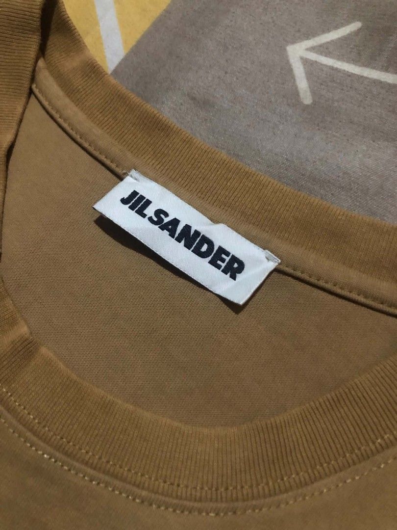 Jil Sander Brown Logo T-Shirt (Category: Shirts) located in Daet. Submitted by quickearth.ac7e7e (Listing ID 1470477095, Image 3). Description: Jil Sander crewneck t-shirt in brown with bold black logo text printed across the chest. Made in Italy from 100% cotton. Standard short sleeve fit. Interior brand tag and care label intact. Hand wash only. Great casual piece for everyday wear..