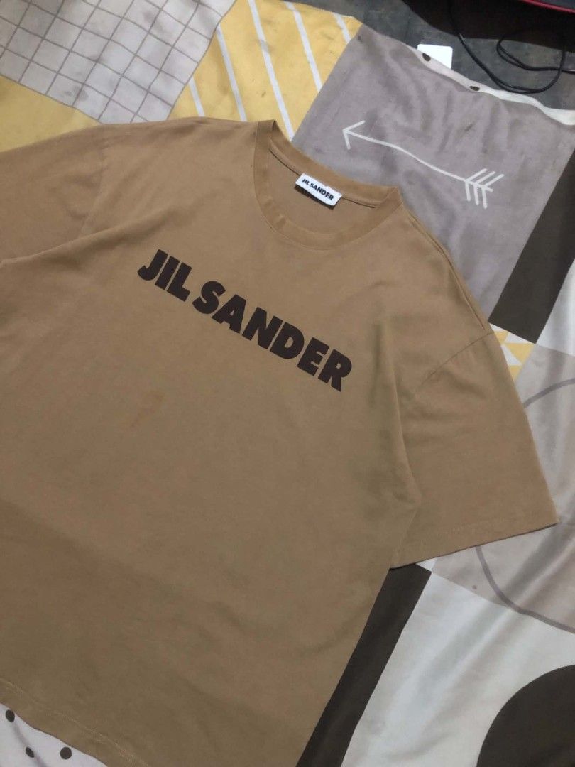 Jil Sander Brown Logo T-Shirt (Category: Shirts) located in Daet. Submitted by quickearth.ac7e7e (Listing ID 1470477095, Image 2). Description: Jil Sander crewneck t-shirt in brown with bold black logo text printed across the chest. Made in Italy from 100% cotton. Standard short sleeve fit. Interior brand tag and care label intact. Hand wash only. Great casual piece for everyday wear..