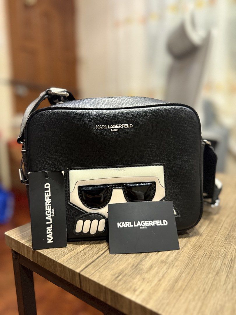 Karl Lagerfeld Paris Black Camera Bag (Category: Cross-body Bags) located in Manila. Submitted by markiverso09561 (Listing ID 1470538482, Image 1). Description: - Brand: Karl Lagerfeld Paris - Material: Black leather - Condition: Brand new with original retail tags attached - Design: Signature character graphic with sunglasses on the front - Storage: Front zip compartment with silver metallic lettering - Strap: Thick woven strap featuring repeati