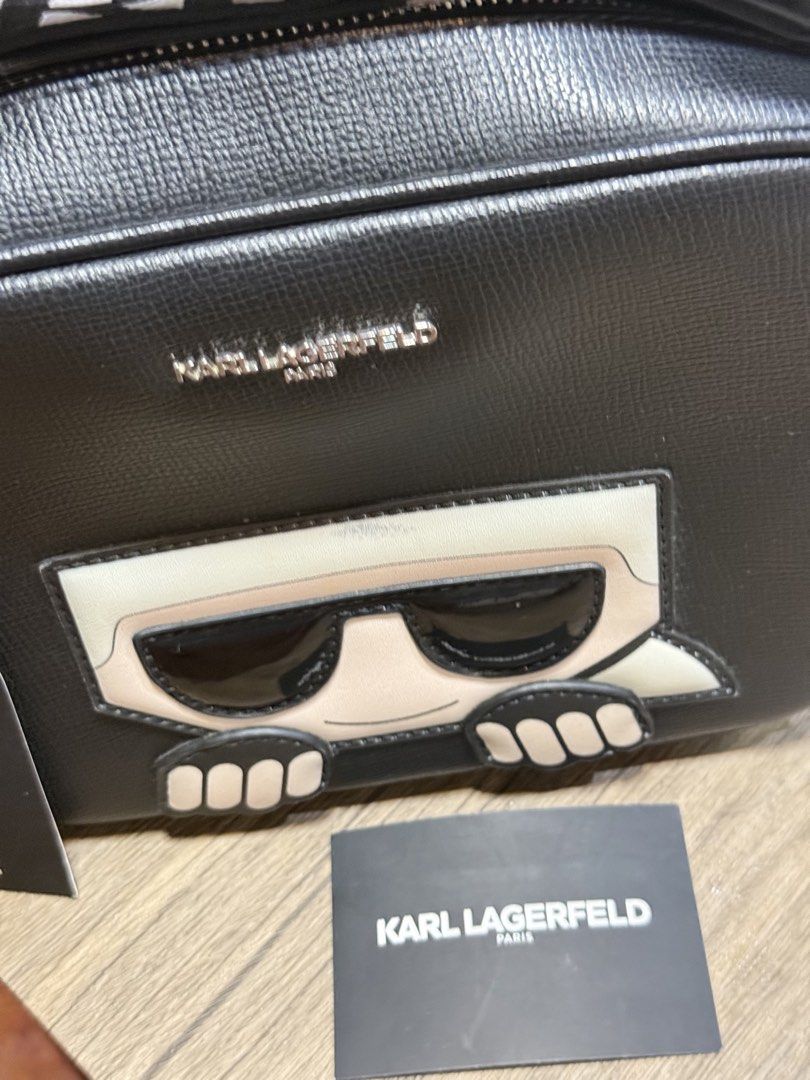 Karl Lagerfeld Paris Black Camera Bag (Category: Cross-body Bags) located in Manila. Submitted by markiverso09561 (Listing ID 1470538482, Image 3). Description: - Brand: Karl Lagerfeld Paris - Material: Black leather - Condition: Brand new with original retail tags attached - Design: Signature character graphic with sunglasses on the front - Storage: Front zip compartment with silver metallic lettering - Strap: Thick woven strap featuring repeati