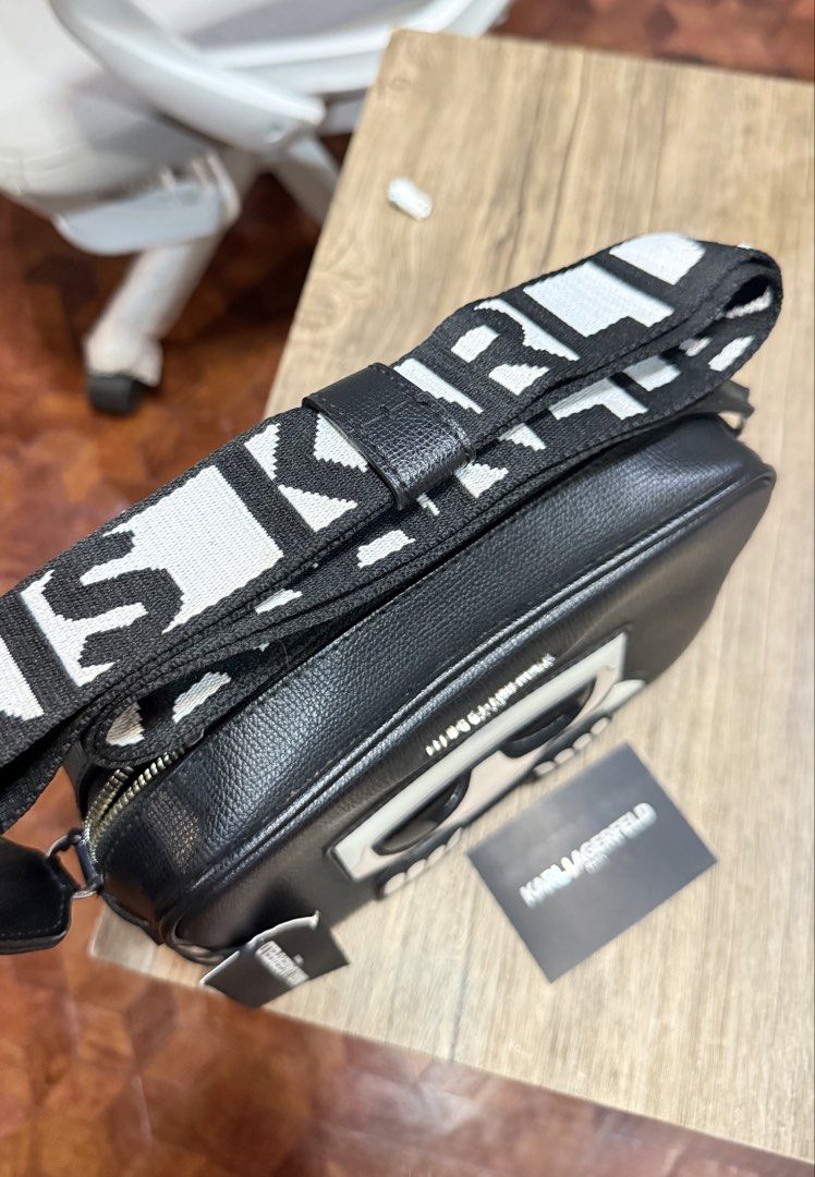 Karl Lagerfeld Paris Black Camera Bag (Category: Cross-body Bags) located in Manila. Submitted by markiverso09561 (Listing ID 1470538482, Image 2). Description: - Brand: Karl Lagerfeld Paris - Material: Black leather - Condition: Brand new with original retail tags attached - Design: Signature character graphic with sunglasses on the front - Storage: Front zip compartment with silver metallic lettering - Strap: Thick woven strap featuring repeati