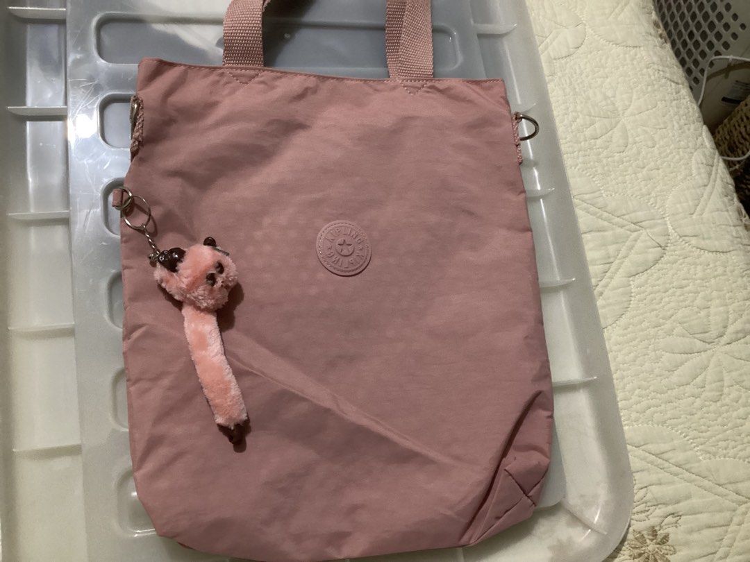 Kipling Pink Tote Bag with Furry Monkey Keychain (Category: Tote Bags) located in Manila. Submitted by peacd (Listing ID 1470482805, Image 1). Description: - Brand: Kipling - Kipling Anina Laptop Tote Bag - Color: Dusty Pink - Material: Lightweight nylon - Inclusions: Signature furry monkey keychain - Features: Circular embossed logo, dual carry handles, hardware rings for a crossbody strap, and a roomy interior - Condition: Clean inside and out 