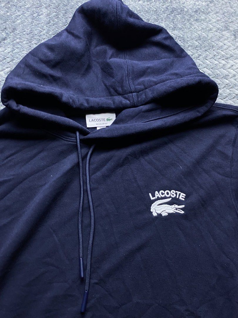 Lacoste Navy Blue Regular Fit Hoodie (Category: Coats, Jackets and Outerwear) located in Olongapo. Submitted by WAVYT (Listing ID 1470552411, Image 2). Description: - Brand: Lacoste - Color: Navy Blue - Size: US XL / French Size 6 (Regular Fit) - Design: Large white embroidered Lacoste text and crocodile logo on the chest - Details: Classic drawstring hood with metal tips, extra small embroidered croc near the bottom hem, and 'French Sportswear e