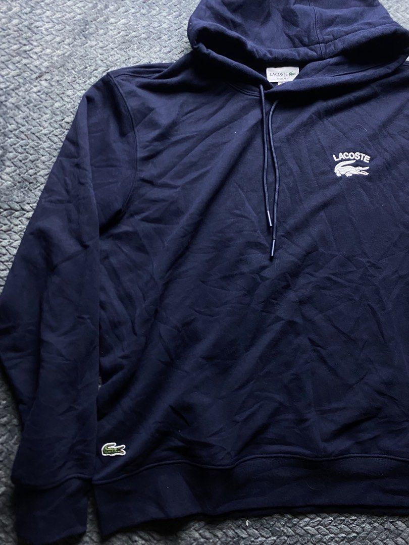 Lacoste Navy Blue Regular Fit Hoodie (Category: Coats, Jackets and Outerwear) located in Olongapo. Submitted by WAVYT (Listing ID 1470552411, Image 3). Description: - Brand: Lacoste - Color: Navy Blue - Size: US XL / French Size 6 (Regular Fit) - Design: Large white embroidered Lacoste text and crocodile logo on the chest - Details: Classic drawstring hood with metal tips, extra small embroidered croc near the bottom hem, and 'French Sportswear e