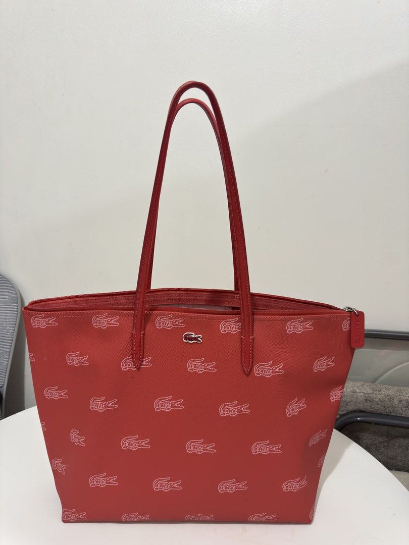 Lacoste Red All-Over Crocodile Monogram Tote Bag (Category: Tote Bags) located in Quezon City. Submitted by decluttergirlie (Listing ID 1470546632, Image 2). Description: - Brand: Lacoste - Style: Red tote bag with all-over white crocodile monogram print - Straps: Double red leather straps with clean stitching - Closure: Top zipper with matching red pull tab - Interior: Light pink lining featuring a white zippered mesh pouch - Condition: Exterior