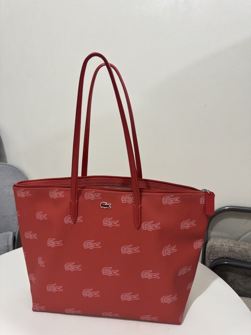 Lacoste Red All-Over Crocodile Monogram Tote Bag (Category: Tote Bags) located in Quezon City. Submitted by decluttergirlie (Listing ID 1470546632, Image 1). Description: - Brand: Lacoste - Style: Red tote bag with all-over white crocodile monogram print - Straps: Double red leather straps with clean stitching - Closure: Top zipper with matching red pull tab - Interior: Light pink lining featuring a white zippered mesh pouch - Condition: Exterior