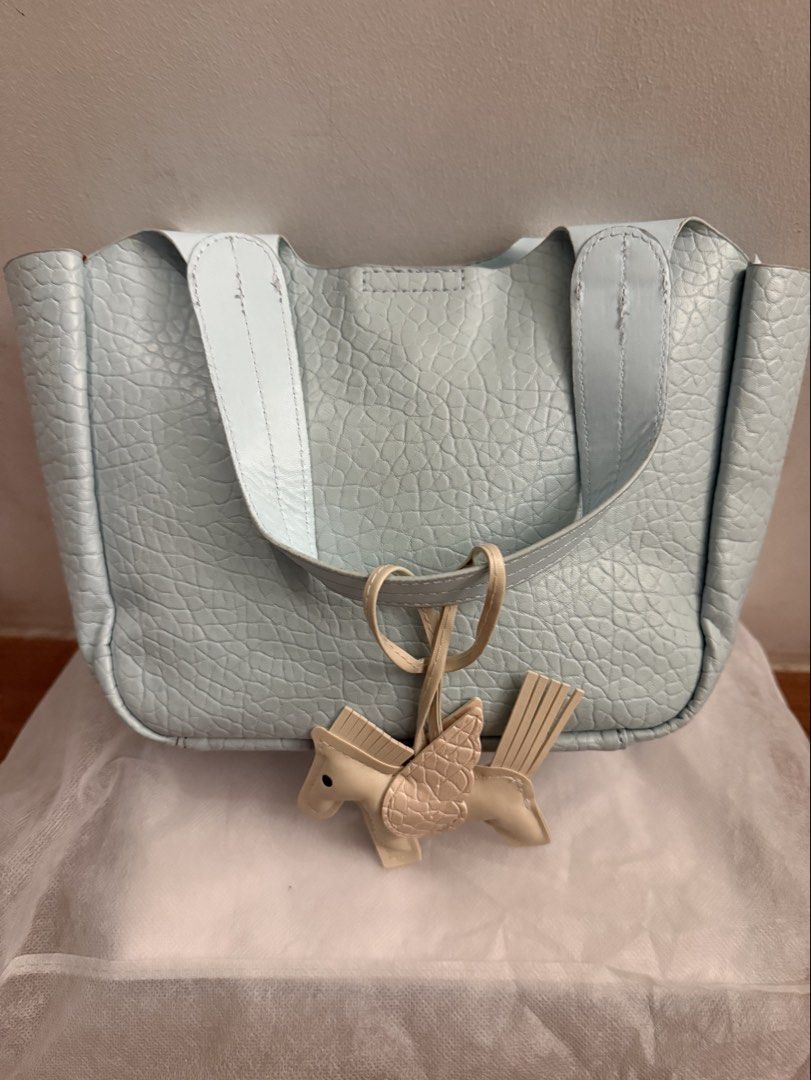 Light Blue Pebbled Leather Tote Bag with Pegasus Charm (Category: Tote Bags) located in Bulacan. Submitted by emjay_17 (Listing ID 1470422866, Image 3). Description: Light blue pebbled leather handbag with double top handles and an extra front strap. Zip-top closure inside. Includes a beige winged horse bag charm dangling from the side. Clean interior stuffed with paper for shape preservation. Great everyday carryall with plenty of room..