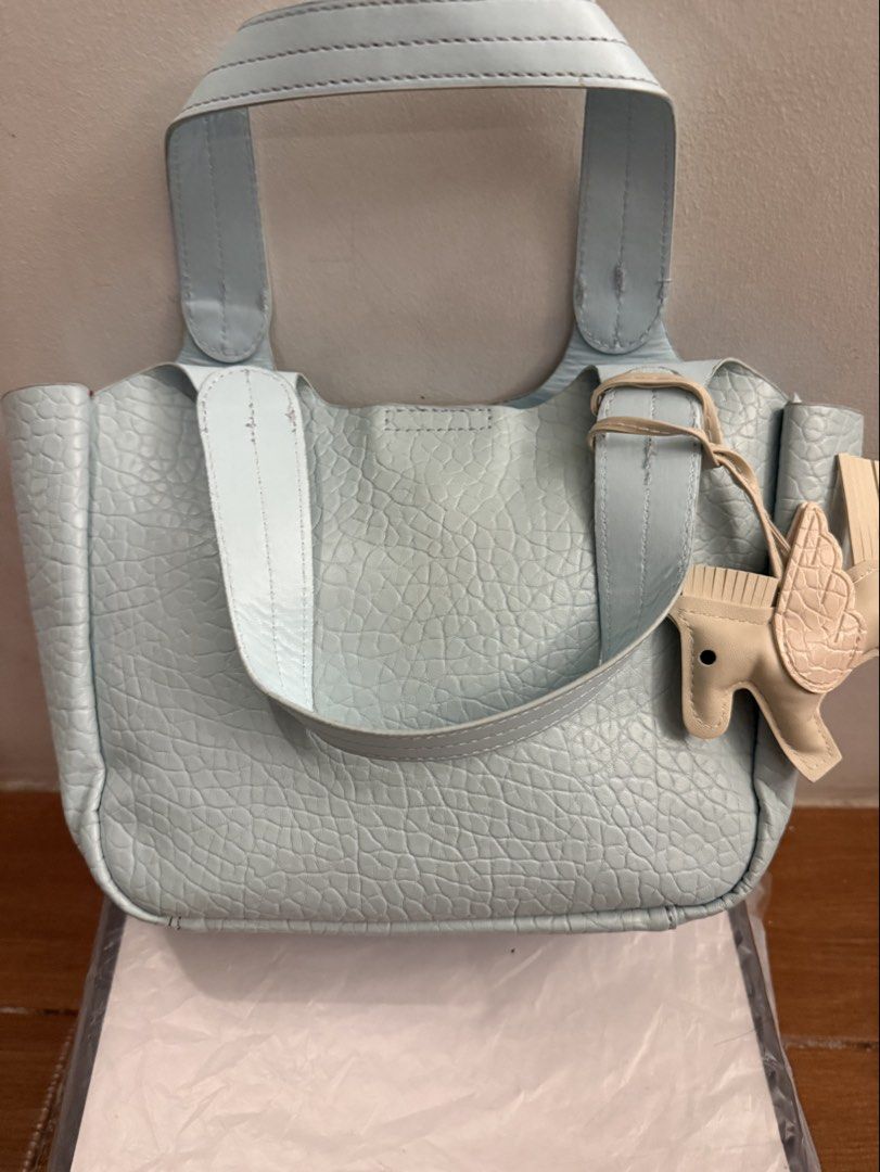 Light Blue Pebbled Leather Tote Bag with Pegasus Charm (Category: Tote Bags) located in Bulacan. Submitted by emjay_17 (Listing ID 1470422866, Image 2). Description: Light blue pebbled leather handbag with double top handles and an extra front strap. Zip-top closure inside. Includes a beige winged horse bag charm dangling from the side. Clean interior stuffed with paper for shape preservation. Great everyday carryall with plenty of room..