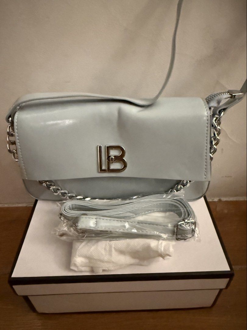 Light blue shoulder bag with chain strap and box (Category: Shoulder Bags) located in Bulacan. Submitted by emjay_17 (Listing ID 1470444272, Image 3). Description: - Color: Light blue with silver-tone hardware - Features: Stylish silver chain side details and large silver LB front lock - Closure: Secure top zipper closure with brown fabric-lined interior - Inclusions: Extra adjustable matching strap (still in plastic packaging) and original box -