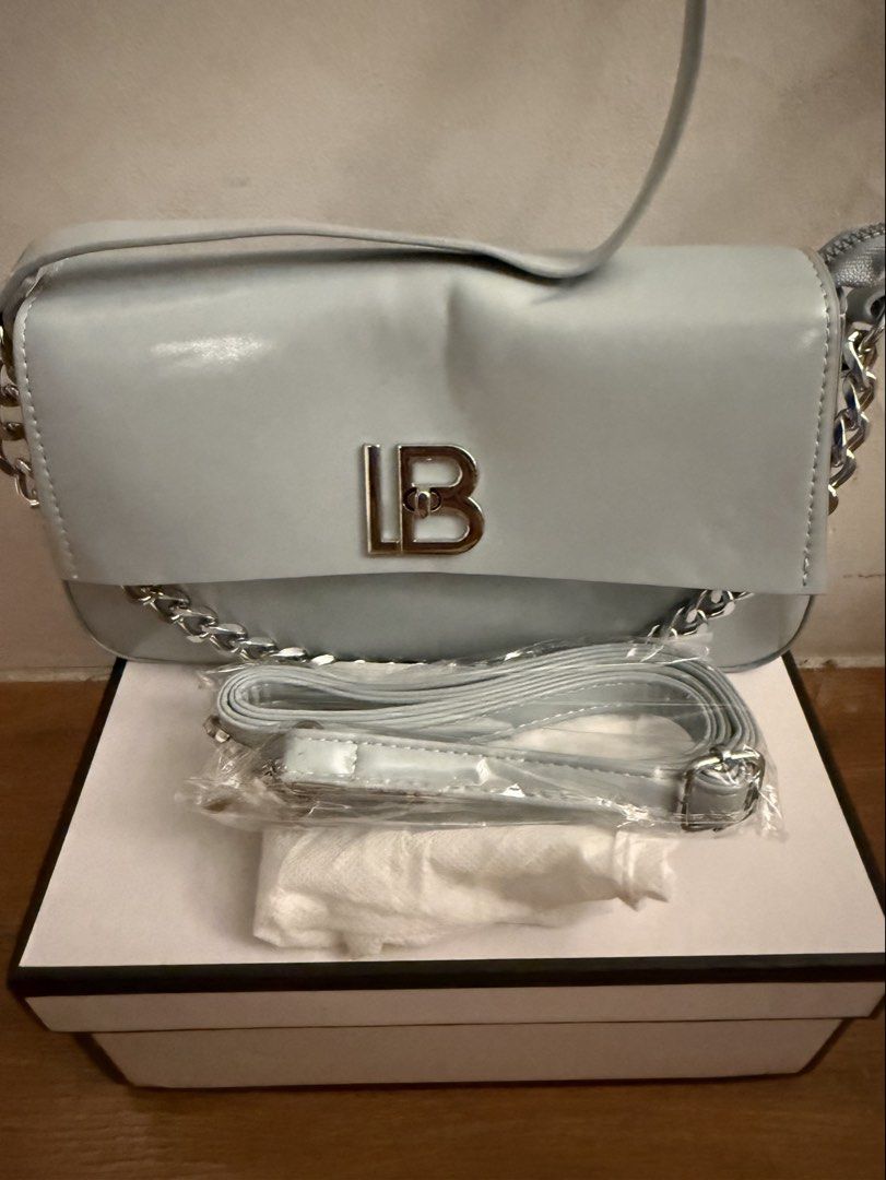 Light blue shoulder bag with chain strap and box (Category: Shoulder Bags) located in Bulacan. Submitted by emjay_17 (Listing ID 1470444272, Image 2). Description: - Color: Light blue with silver-tone hardware - Features: Stylish silver chain side details and large silver LB front lock - Closure: Secure top zipper closure with brown fabric-lined interior - Inclusions: Extra adjustable matching strap (still in plastic packaging) and original box -