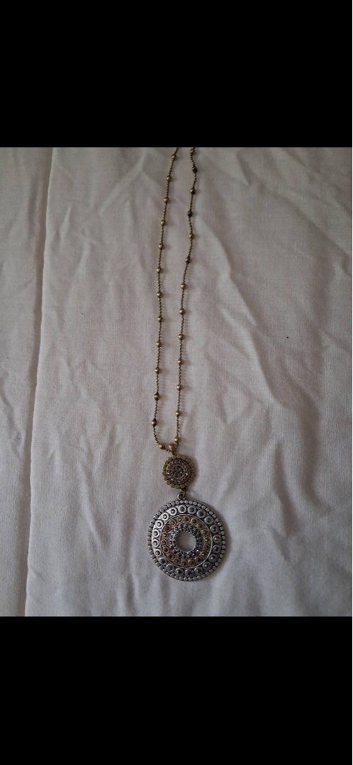 Long chain necklace with round patterned pendant (Category: Necklaces) located in Muntinlupa City. Submitted by everythingmustgo_8475da (Listing ID 1470484531, Image 1). Description: - Style: Bohemian, earthy tones - Design: Long beaded chain with station details - Pendant: Large mixed-metal circular medallion in silver, bronze, and dark metal - Connector: Textured circle link - Versatility: Perfect for casual outfits or dressing up plain tops - 