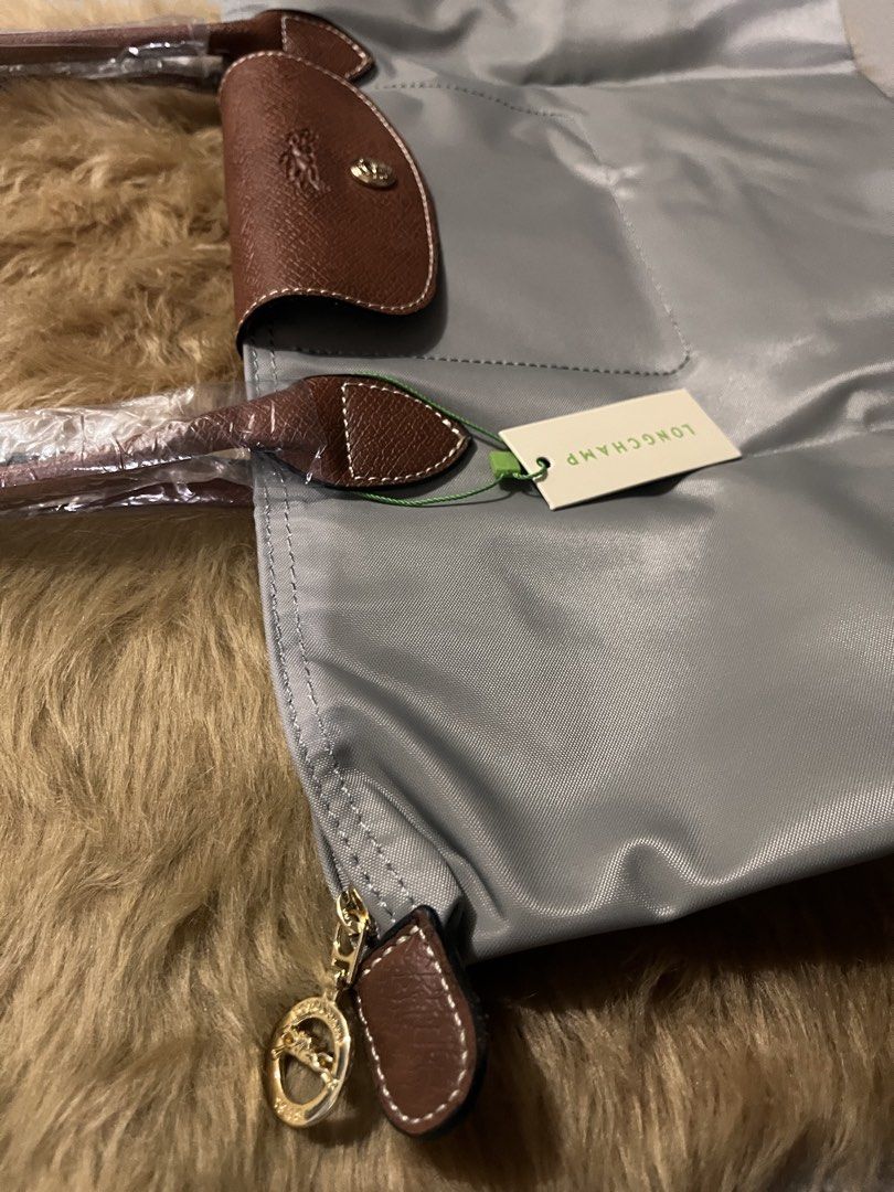 Longchamp Le Pliage Grey Tote Bag (Category: Luxury Bags & Wallets) located in Quezon City. Submitted by pickleballpaddle (Listing ID 1470528389, Image 3). Description: - Authentic Longchamp Le Pliage tote bag in a versatile grey shade - Brand new and unused condition with tags attached - Features brown leather trim, top handles, and front flap with snap closure - Gold-tone zipper pull with signature horse emblem - Handles are still wrapped in or