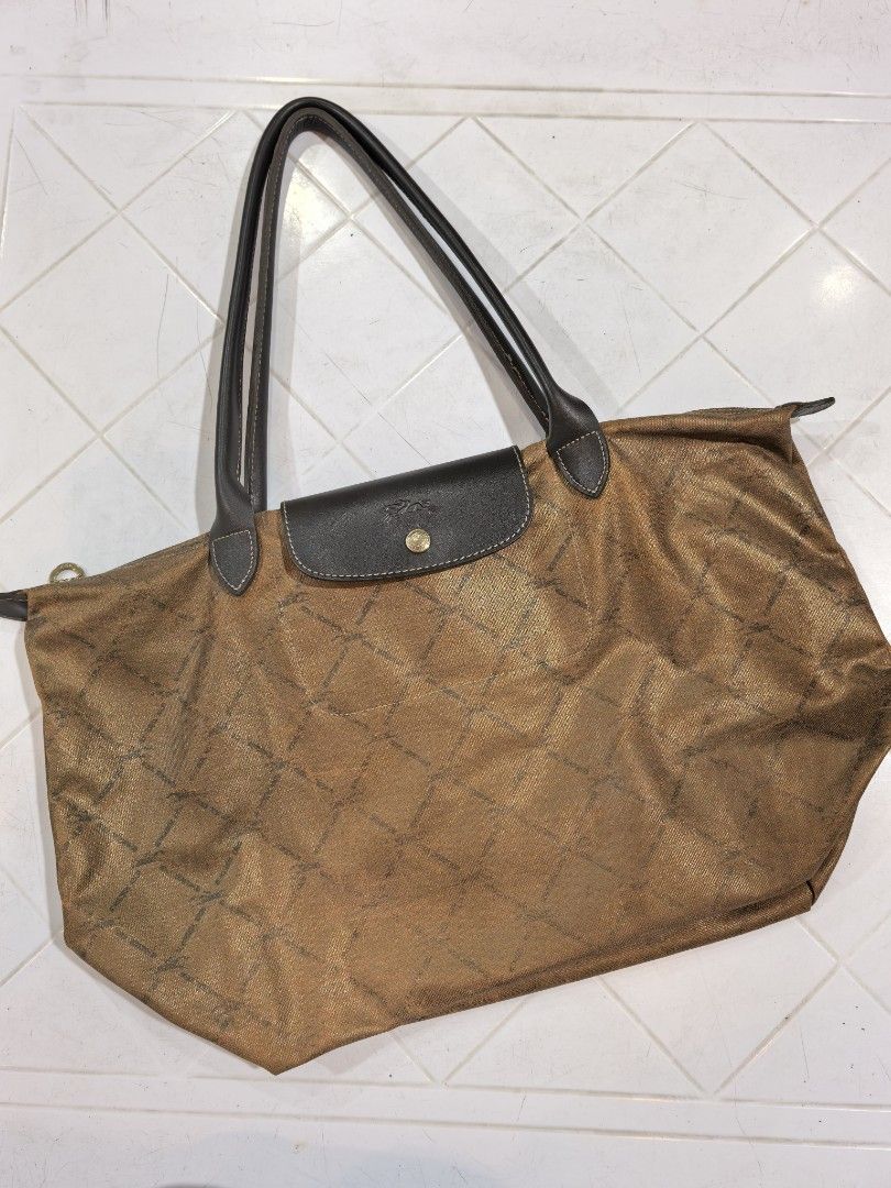 Longchamp Paris Bronze Tote Bag (Category: Luxury Bags & Wallets) located in Manila. Submitted by jsu2026 (Listing ID 1470500211, Image 1). Description: Longchamp Paris tote bag in metallic bronze with a geometric grid pattern. Dark brown leather handles and flap closure with gold-tone snap button. Zipper closure with horse medallion pull. Interior tag reads Longchamp Paris, Made in France. Spacious interior compartment with brown lining..