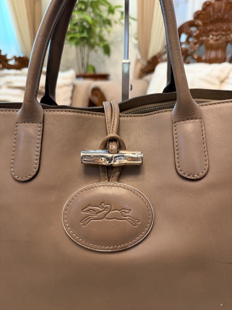 Longchamp Roseau Leather Heritage Bag (Category: Tote Bags) located in Santiago. Submitted by yrellagnoihsaf (Listing ID 1470382497, Image 2). Description: ORIG Longchamp Roseau Heritage leather tote bag in a clay or taupe/beige color, featuring dual rolled handles, silver-tone hardware, an embossed oval logo on the front, and the signature bamboo-accented toggle closure. Normal signs of usage no rips no hole. 🌷.