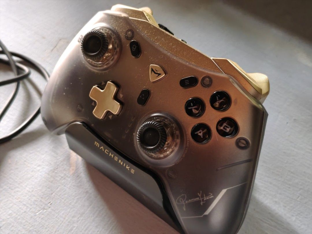 Machenike G5 Pro V2 Gaming Controller with Charging Dock (Category: Controllers) located in Manila. Submitted by mchester14887 (Listing ID 1470492229, Image 3). Description: - Model: Machenike G5 Pro V2 controller - Colorway: Dark translucent grey and gold - Accessories included: Matching charging dock stand and USB cable - Compatibility: Works across multiple platforms (PC/console) - Condition: Clean body with minimal signs of handling - Perform