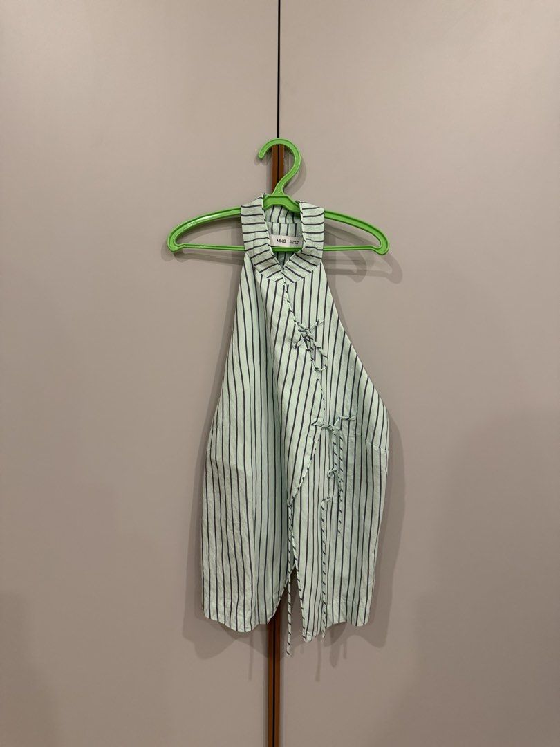 MANGO (MNG) Striped Halter Wrap Top (Category: Sleeveless) located in Muntinlupa City. Submitted by closet.natalia (Listing ID 1470478365, Image 2). Description: MANGO (MNG) Striped Halter Wrap Top ● Brand: MANGO (MNG) ● Color: Light mint green with dark stripes ● Vertical pinstripe pattern ● Halter neckline with collar detail ● Wrap-style front with adjustable side ties ● Asymmetrical pointed hem 📌 Payment: GCash, BPI bank transfer, or PayPal O