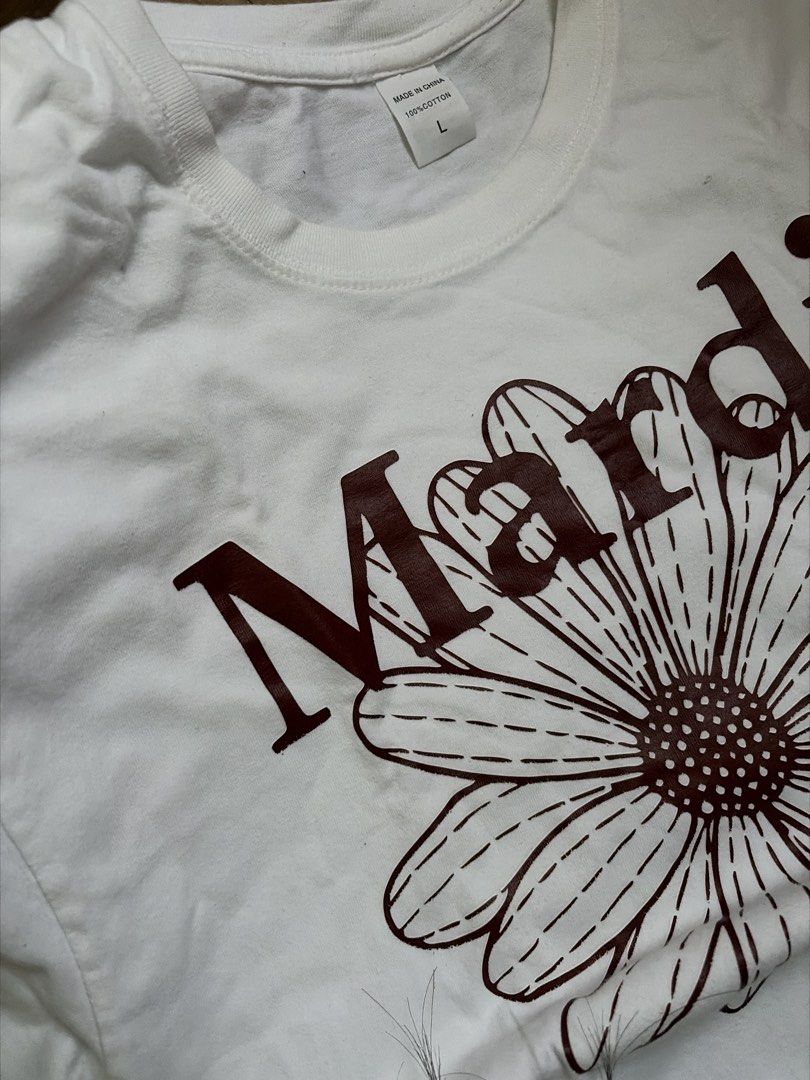 Mardi Shirt (Category: Shirts) located in Taguig. Submitted by nics04433 (Listing ID 1470372922, Image 2). Description: - Brand: Mardi Mercredi - Color: White with large brown flower & brand graphic - Size: L - Material: 100% cotton - Condition: Good, worn a few times - Details: Short sleeves, crew neck, made in China - Style: Versatile basic, perfect with jeans or shorts.