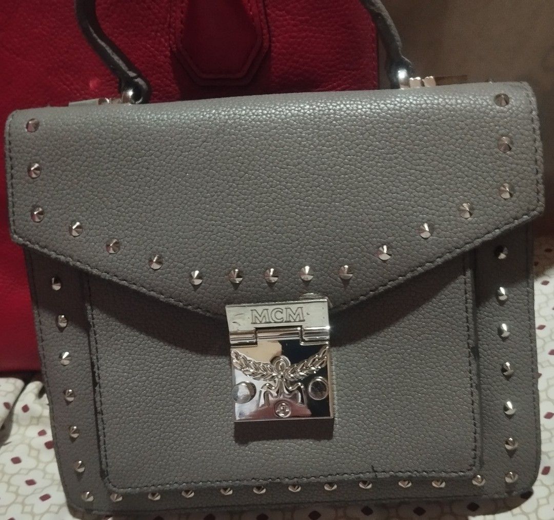 MCM Gray Leather Studded Crossbody Bag (Category: Cross-body Bags) located in Manila. Submitted by lene48 (Listing ID 1470505735, Image 1). Description: Gray pebbled leather bag from MCM. Silver tone hardware and studded details along the edges. Flap top closure with a push lock clasp. Comes with a matching adjustable shoulder strap. Compact size for daily essentials. Clean interior and structured shape..