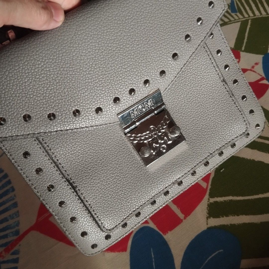 MCM Studded Grey Leather Satchel Handbag (Category: Cross-body Bags) located in Manila. Submitted by lene48 (Listing ID 1470349755, Image 2). Description: - MCM bag in grey pebbled leather - Chic silver-tone stud detailing along the flap and edges - Secure metal push-lock closure with engraved logo - Vibrant bright orange interior lining with a zipped pocket and silver brand plaque - Compact, structured top-handle design - Made in Italy, small si